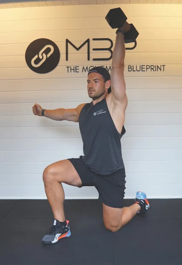 Man in a gym performing a single-arm dumbbell press