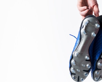 Football soccer player holding football boots cleats in hand on white background with copy space.