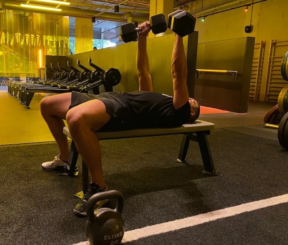 Man in a gym performing a dumbbell bench press