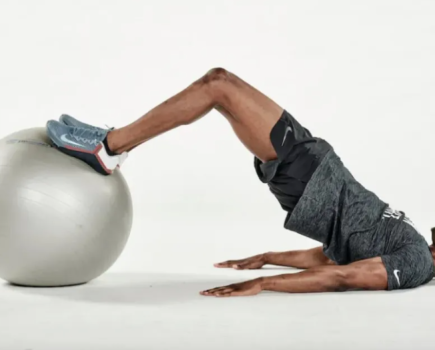 Man lying on the floor performing an exercise ball hamstring curl