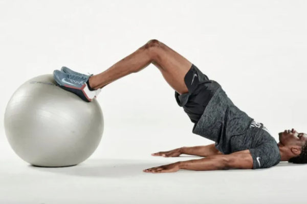 Man lying on the floor performing an exercise ball hamstring curl