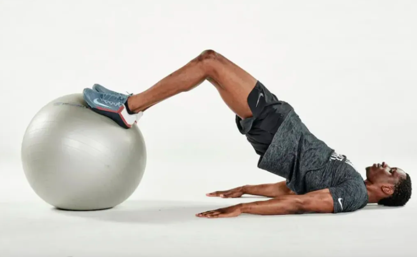 Man lying on the floor performing an exercise ball hamstring curl