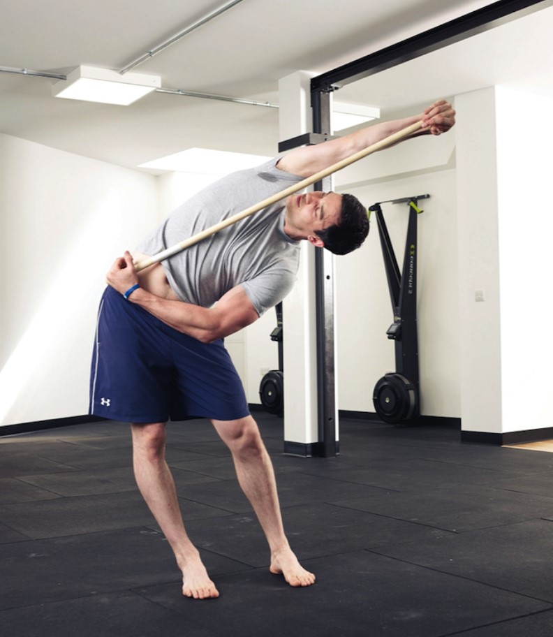 Man performing a lat stretch exercise with a stick