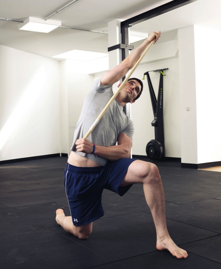 Man performing a lat stretch exercise with a stick