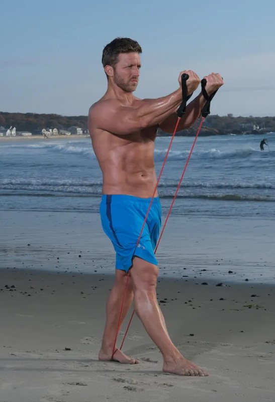 Man performing a resistance band low-to-high on a beach