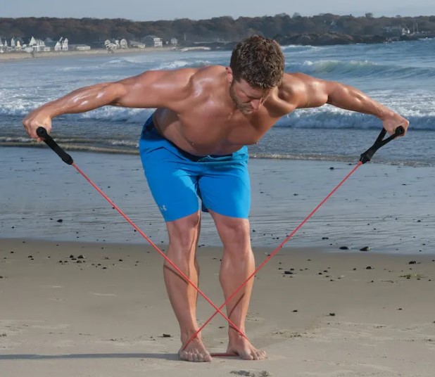 Man on a beach performing a banded bent-over row