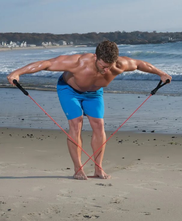 Man performing a resistance band reverse flye on a beach