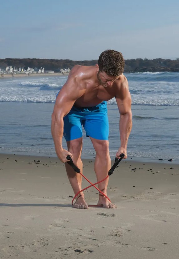 Man performing a resistance band reverse flye on a beach