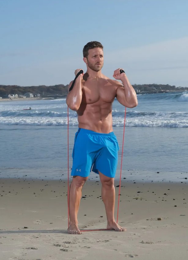 Man performing a resistance band squat on a beach