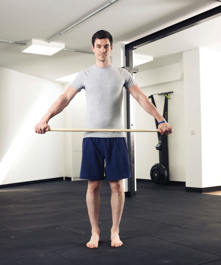 Man performing a shoulder 'dislocation' exercise with a stick