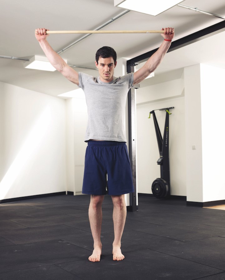 Man performing a shoulder 'dislocation' exercise with a stick