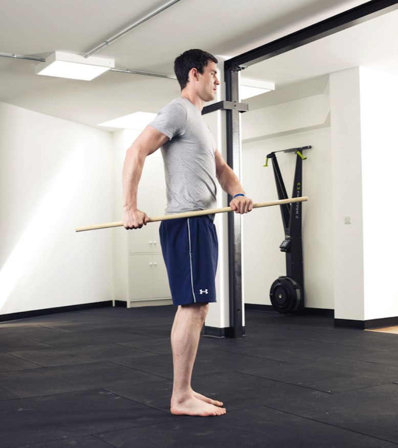 Man performing a side rotation exercise with a stick