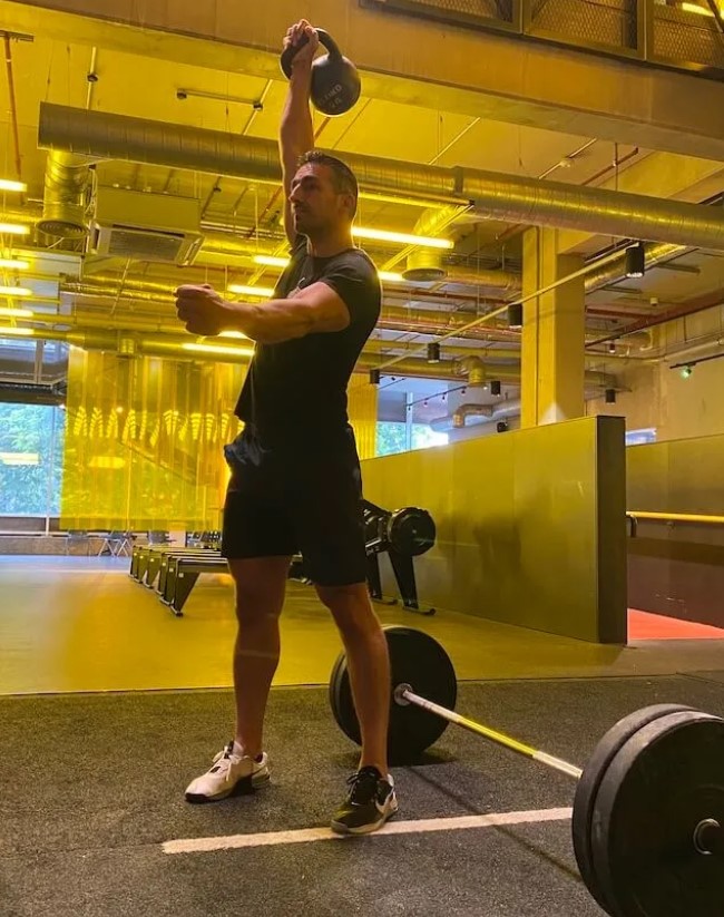 Man in a gym performing a single-arm kettlebell press