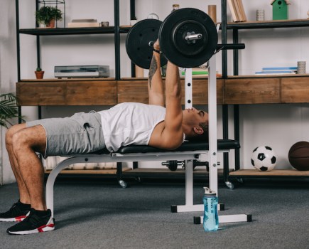 Man using a barbell and weights bench at home