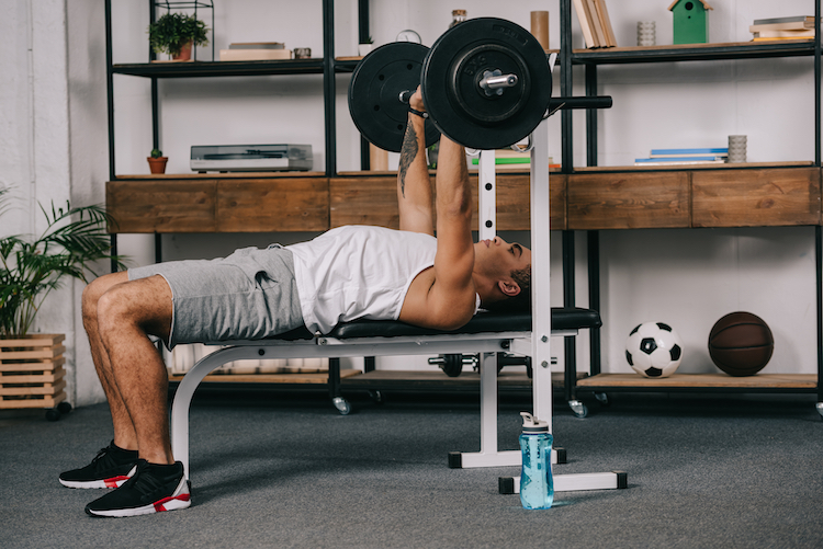 Man using a barbell and weights bench at home