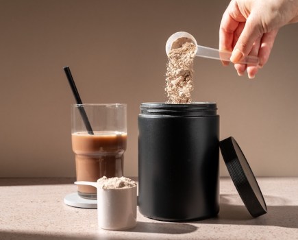 A hand pouring a scoop of protein powder into a tub