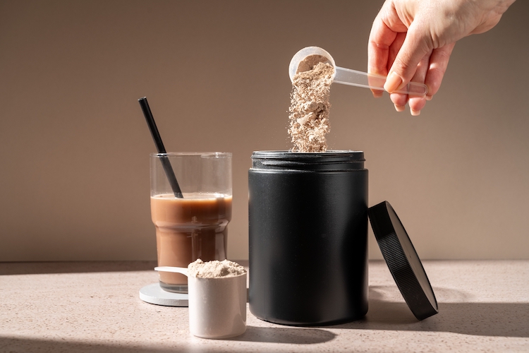 A hand pouring a scoop of protein powder into a tub