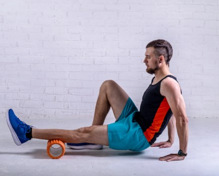 Man sitting down rolling a foam roller along his calf