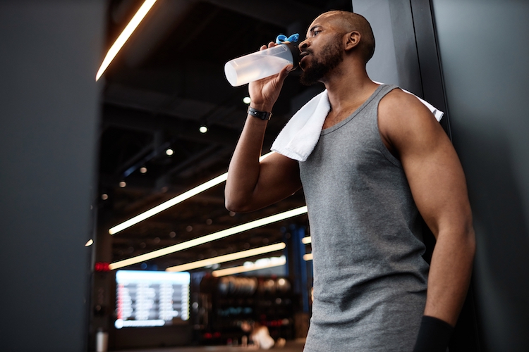 A man leaning against a gym wall drinking