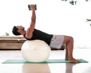 Man lifting weights on an exercise ball at home