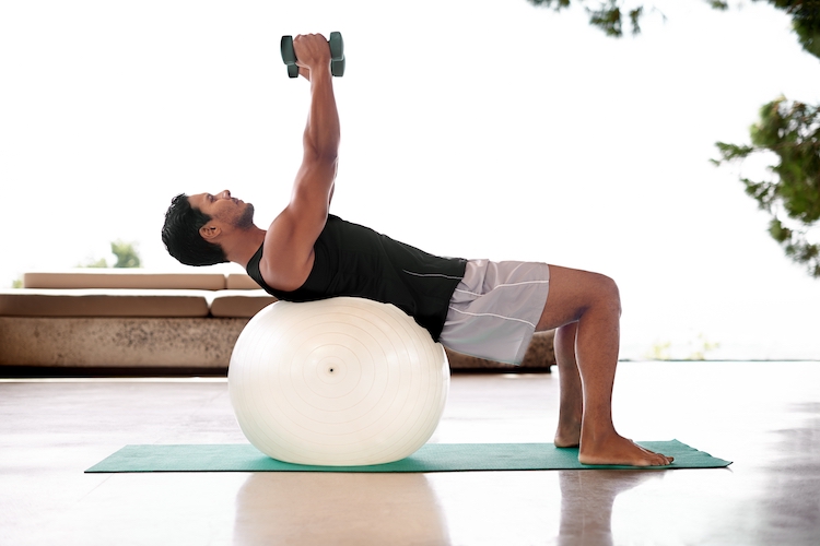 Man lifting weights on an exercise ball at home