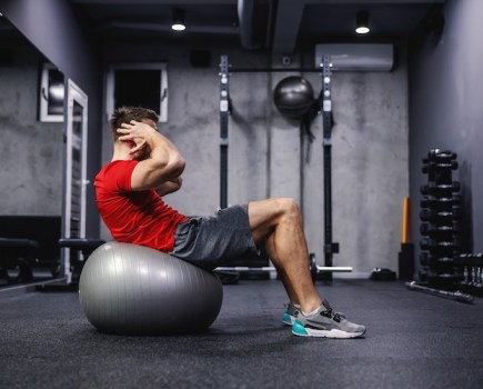 Man in a gym doing crunches on an exercise ball