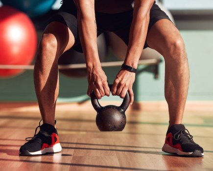 Close-up of a man's feet as he squats to lift a kettlebell