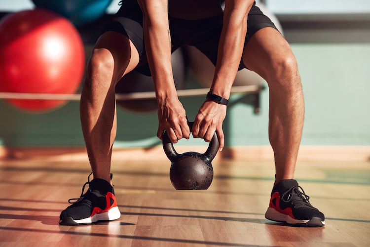 Close-up of a man's feet as he squats to lift a kettlebell