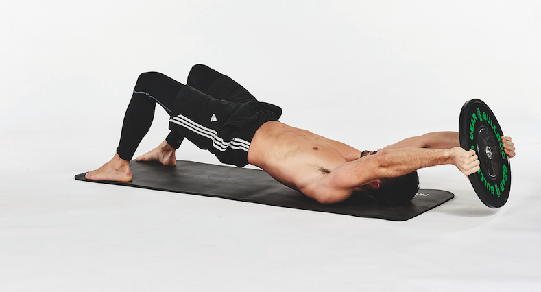 Man lying on a mat performing a plate bridge pullover