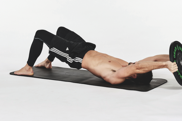 Man on a mat performing exercises with a weight plate