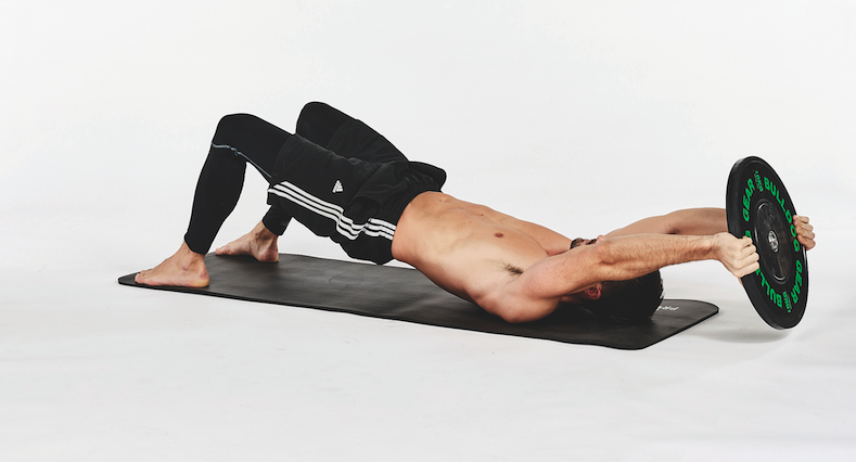 Man on a mat performing exercises with a weight plate