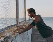 Runner leaning against a fence by the sea