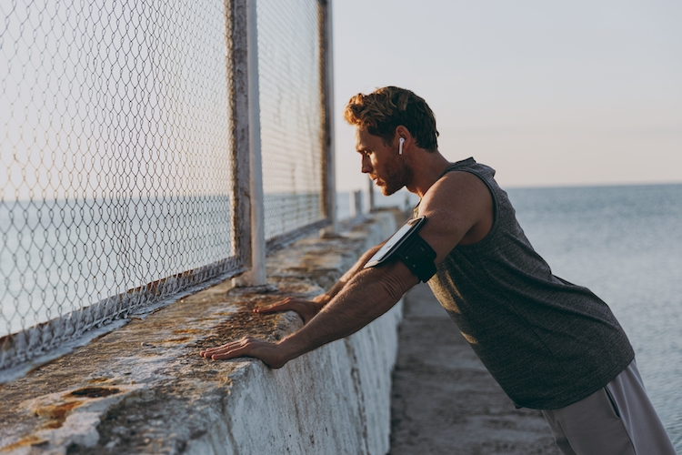 Runner leaning against a fence by the sea