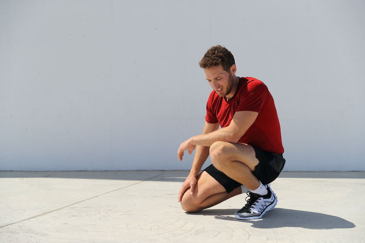 A tired male runner kneeling and recovering