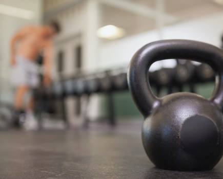 Kettlebell in the foreground; man choosing kettlebells in the background