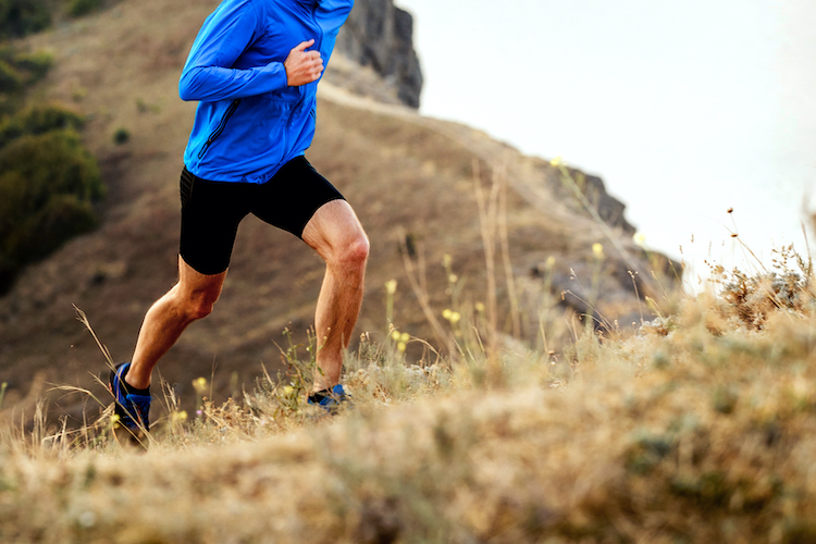 Lower torso of a man running up a hill in shorts