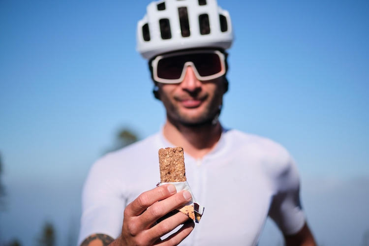 A male cyclist holding up a protein bar