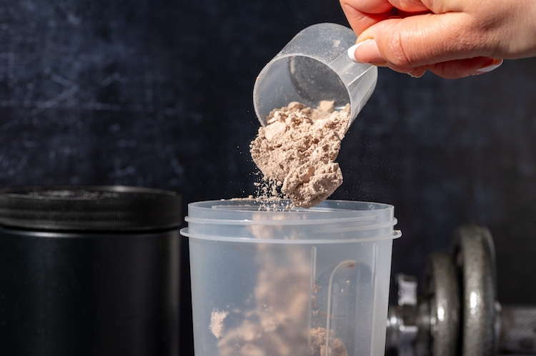 Close-up of a scoop of protein powder being poured into a beaker