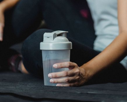 woman holds clear protein powder in a bottle