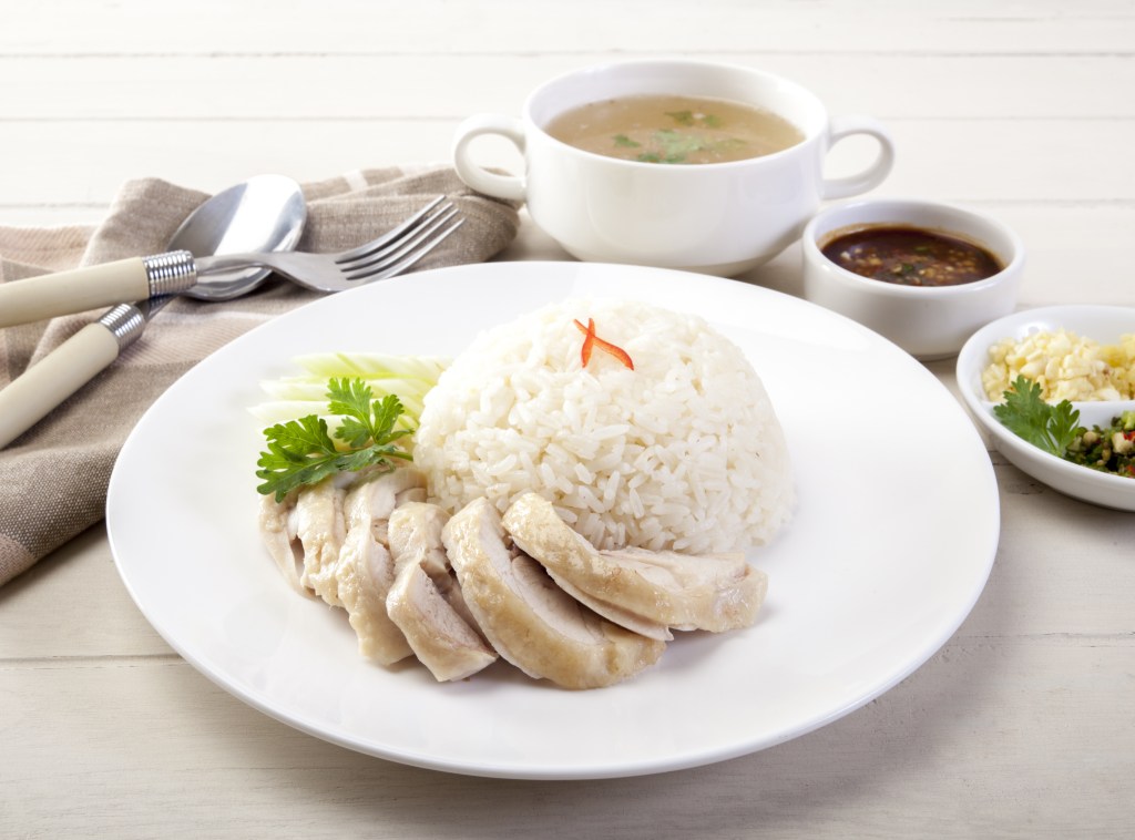 A white dish with chicken and rice on a white tbale with side dishes and cutlery