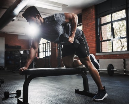 Man performing dumbbell exercises on a weight bench in a gym
