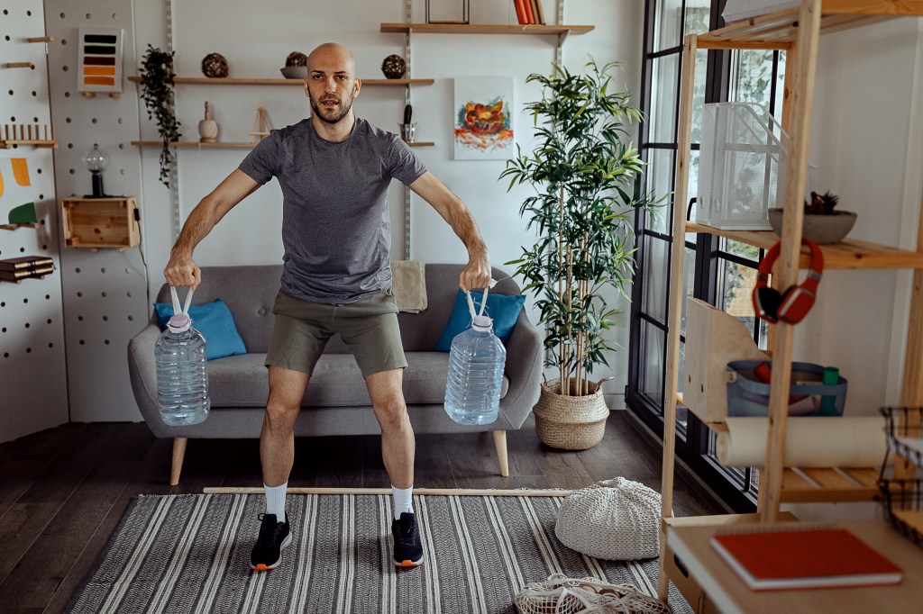 Young man exercising with a gallons of water at home