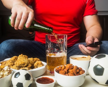Close-up of a man pouring beer and eating snacks while watching football