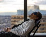 A man reclining in a chair from right to left in an office building during the working day wearing an eye mask to help him de-stress