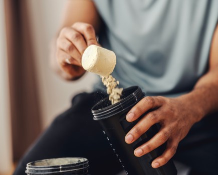 Person scooping creatine into protein shake bottle