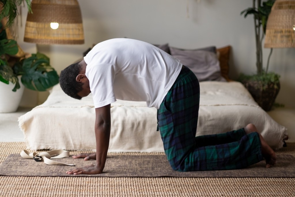 Man performing a cat cow yoga move in a bedroom