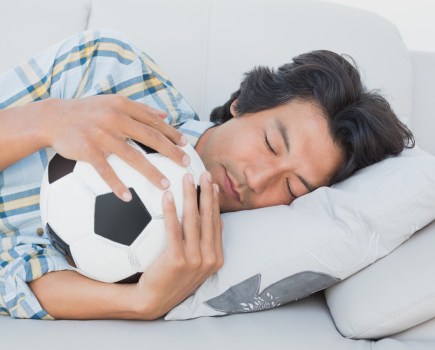 Football fan sleeping on couch hugging ball